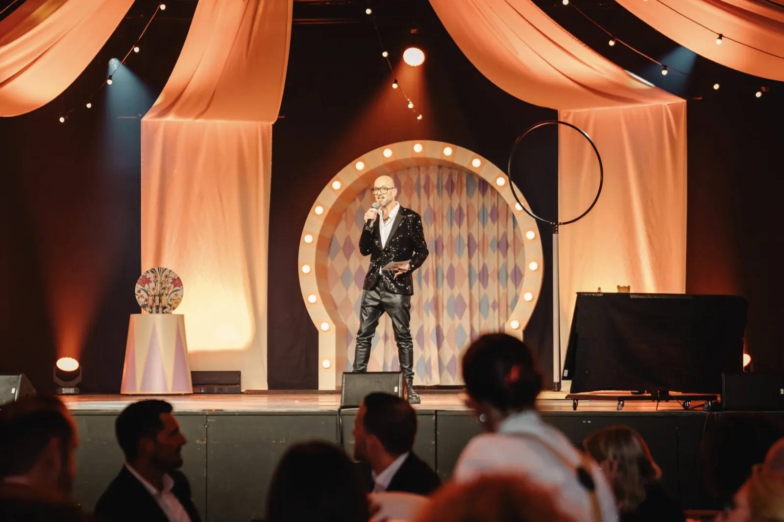 Ein Moderator im glitzernden Sakko spricht auf einer Bühne vor Publikum — Cirque Inspiré im Maritim Hotel Würzburg