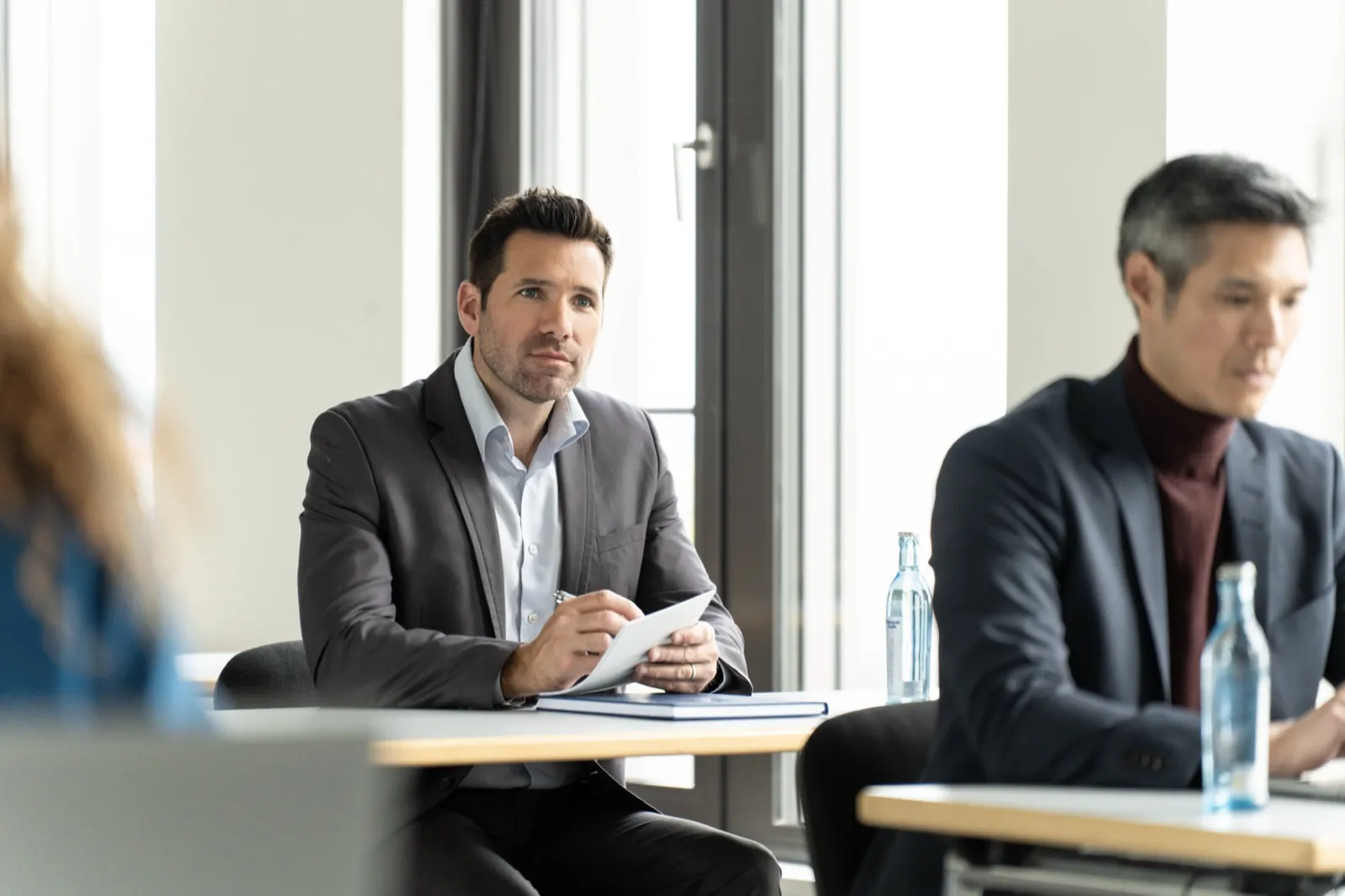 Zwei Männer im Business-Anzug sitzen aufmerksam an Tischen während einer Konferenz — Frankfurt School